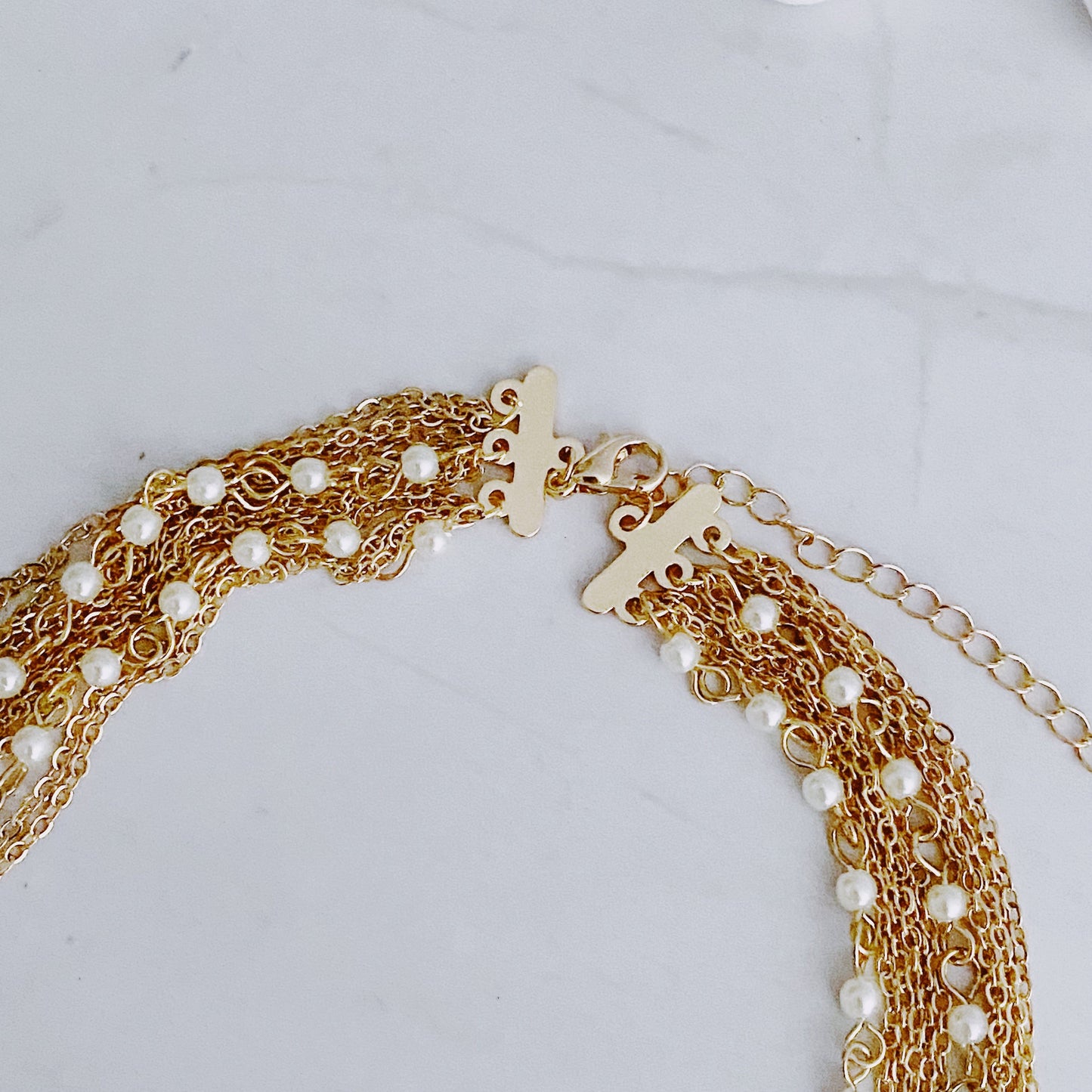 The Beautifully Draping Pearl and Chain Necklace by Ellison + Young is elegantly displayed on a white surface, showcasing its intricate chain designs.