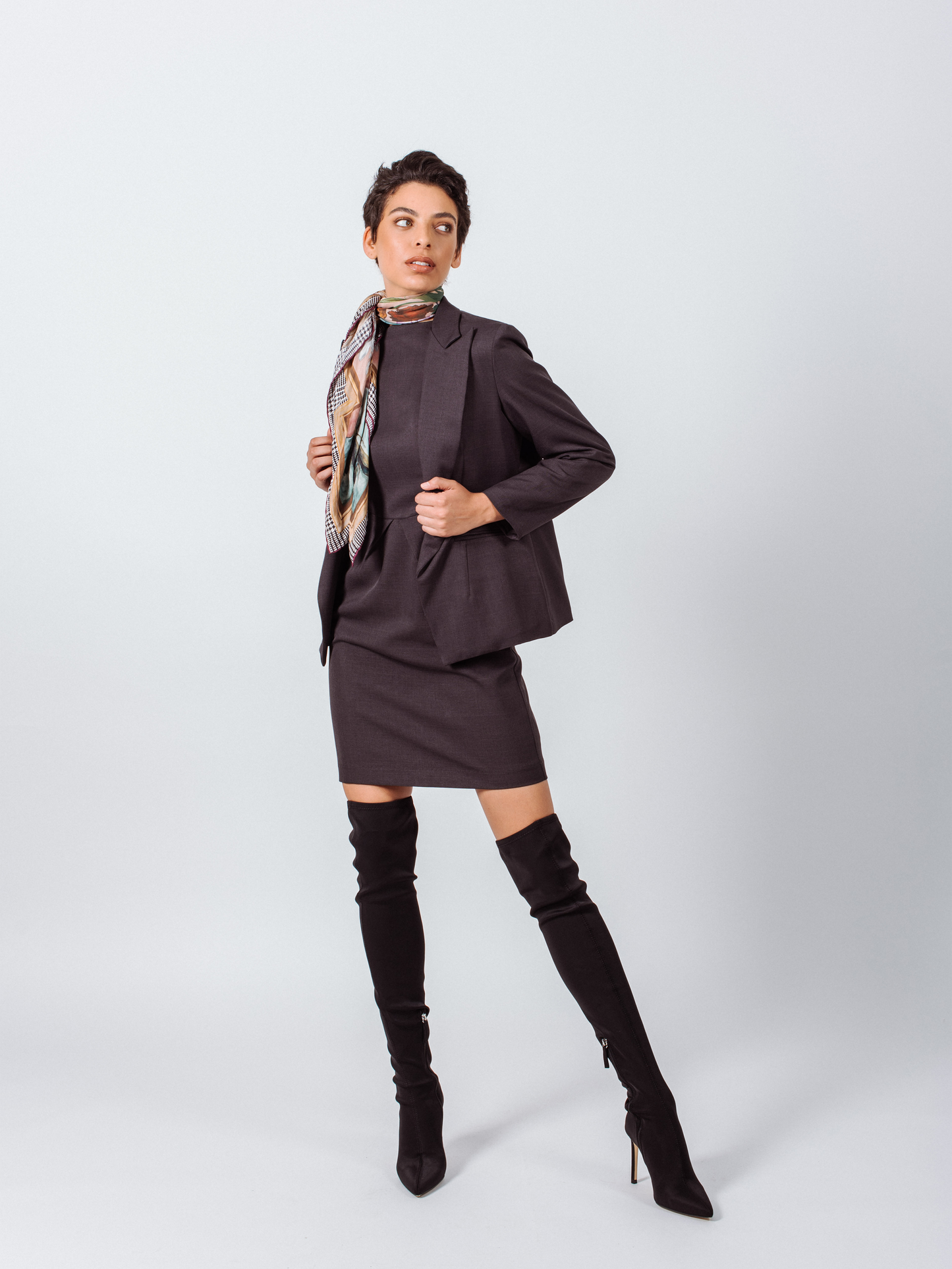 Someone wearing a Le Réussi® Classy Charcoal Wool Blazer and knee-high boots, accentuated with a patterned scarf, poses against a plain backdrop.