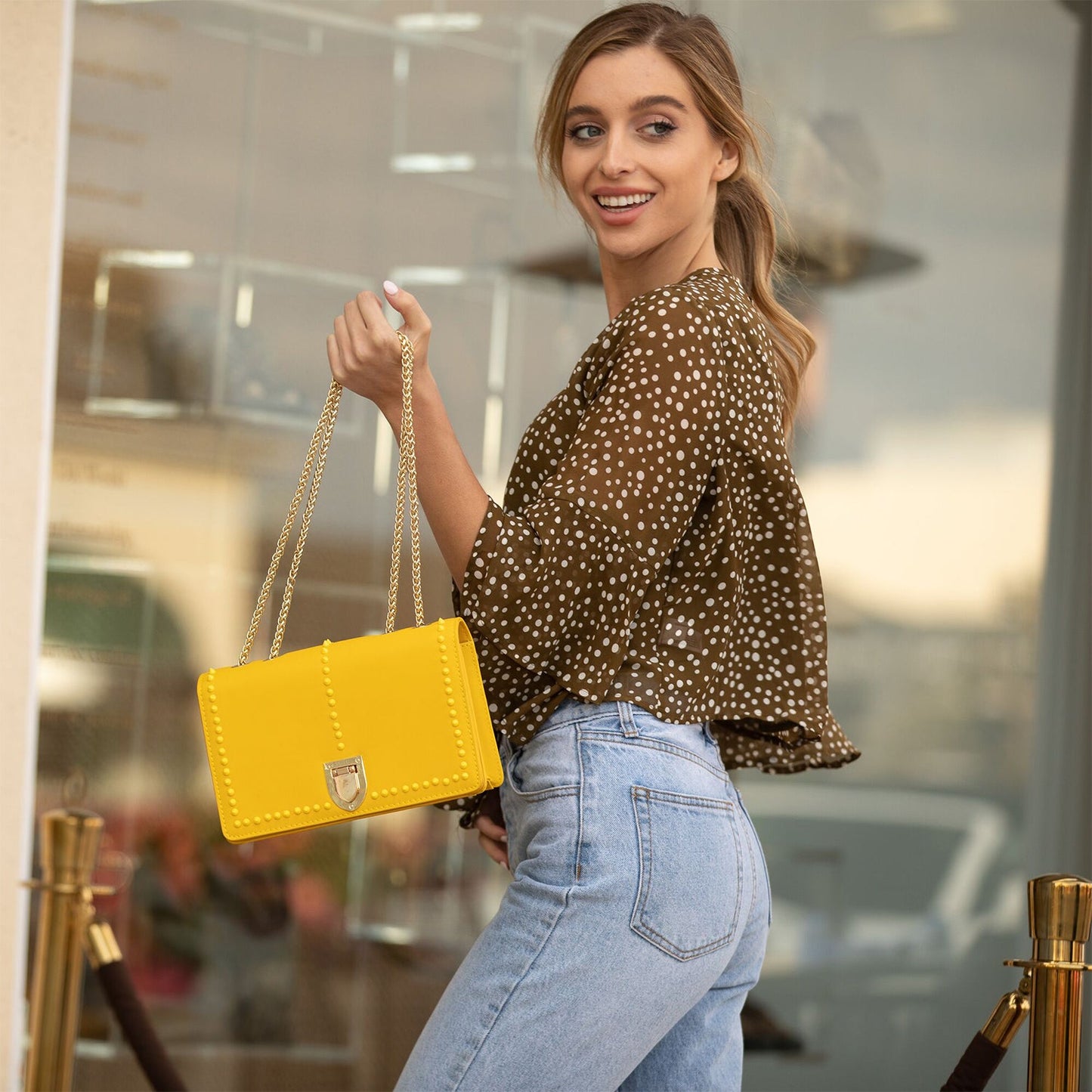 The SUSU Josie Mustard Yellow Leather Purse features gold chain straps, a clasp, and a front row of small studs.