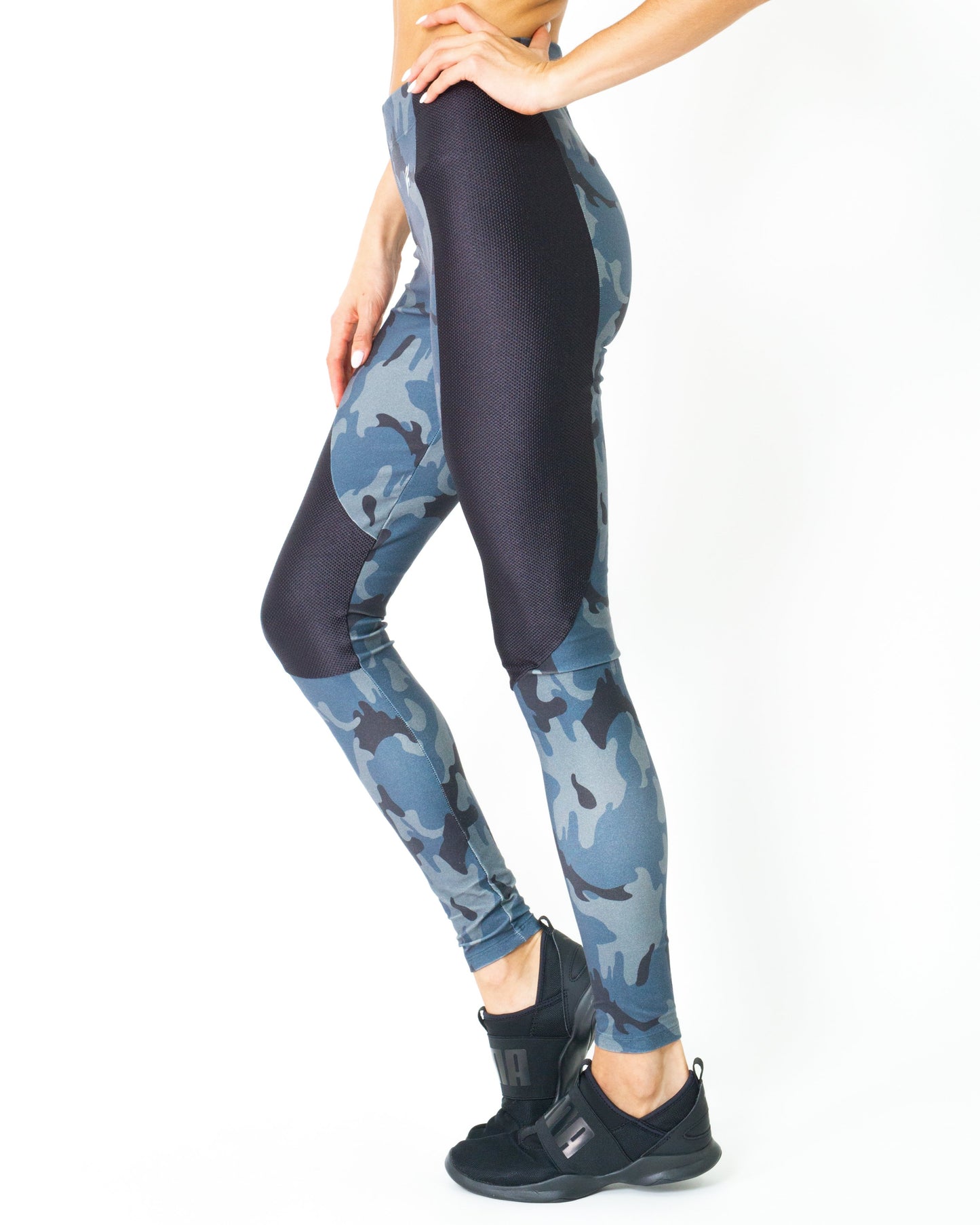Wearing the Veloso Supplex Moisture-Resistant Fashion Leggings & Sports Bra Set by Savoy Active, a person in camo-patterned workout attire poses indoors with one hand on a swinging chair.