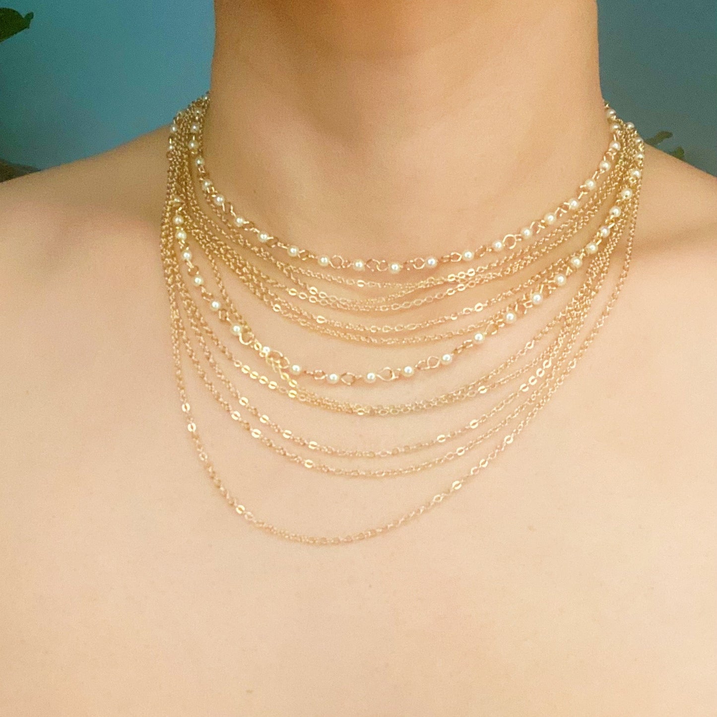 The Beautifully Draping Pearl and Chain Necklace by Ellison + Young is elegantly displayed on a white surface, showcasing its intricate chain designs.
