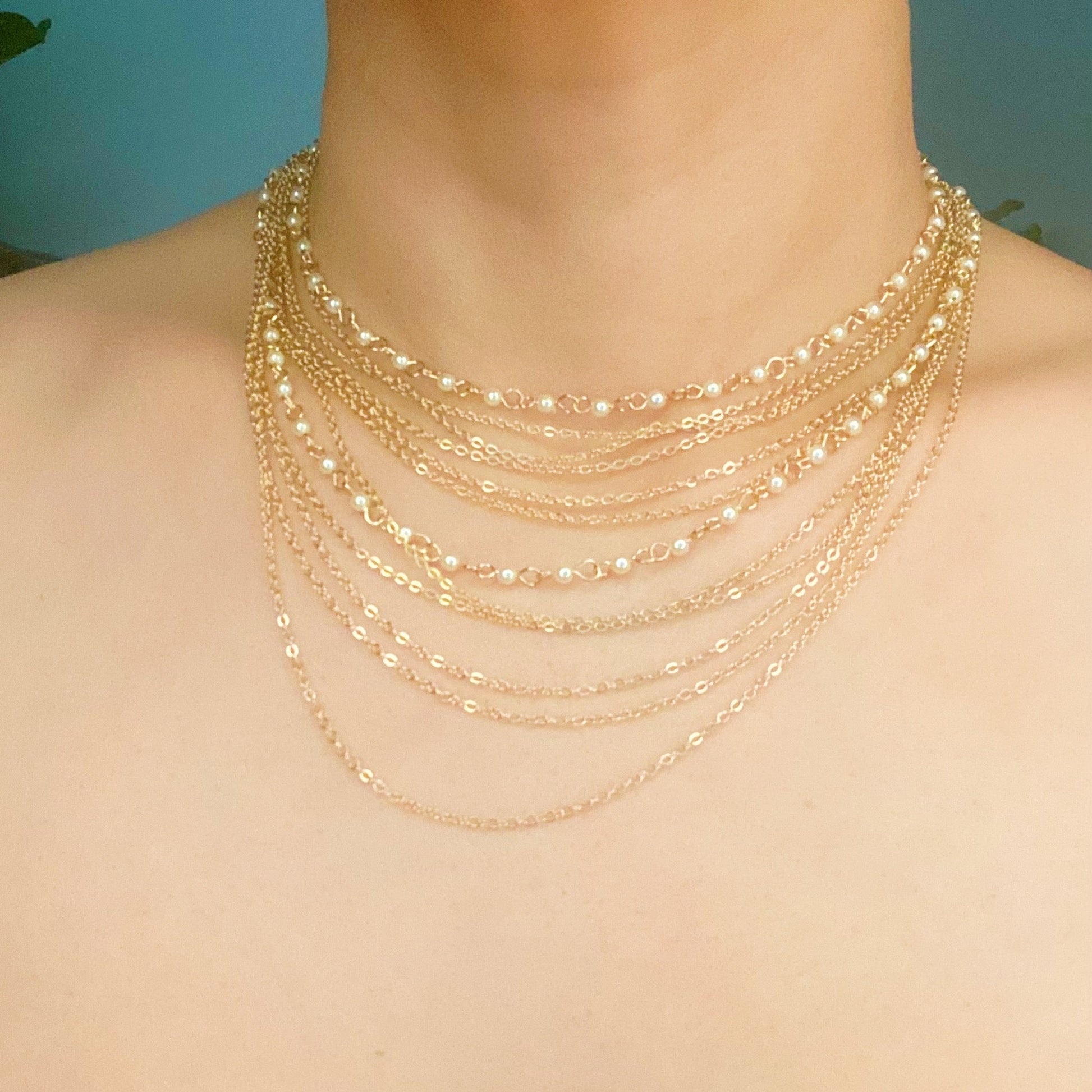 The Beautifully Draping Pearl and Chain Necklace by Ellison + Young is elegantly displayed on a white surface, showcasing its intricate chain designs.