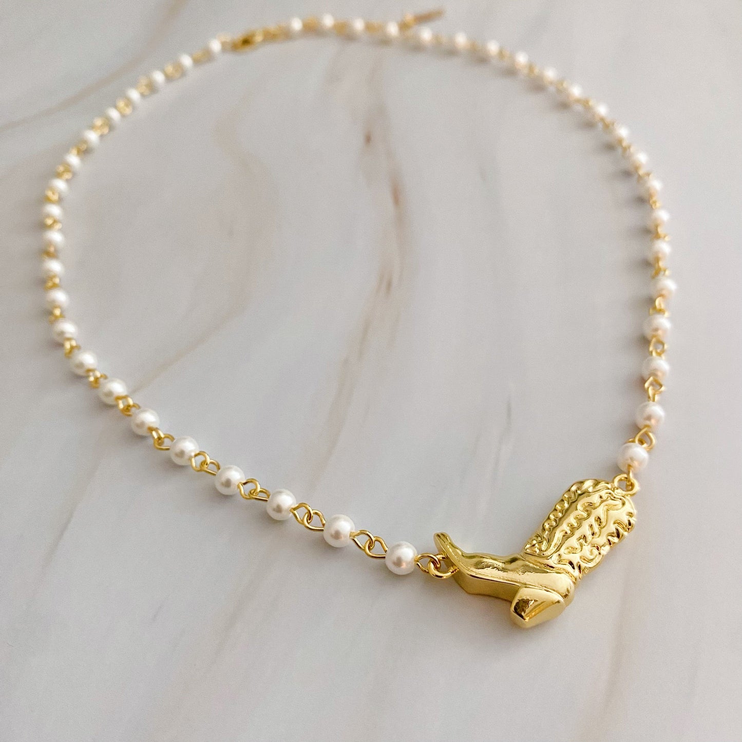 Ellison + Youngs Cowgirl Boot Pearl Chain Necklace is displayed on a marble surface.
