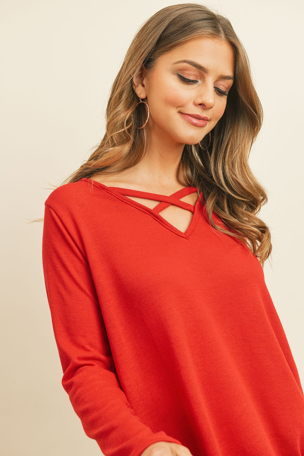 A person wearing a Riah Fashion Criss Cross Neck Long Sleeve Hacci Top in Dusty Blush and blue jeans stands against a neutral background, smiling.