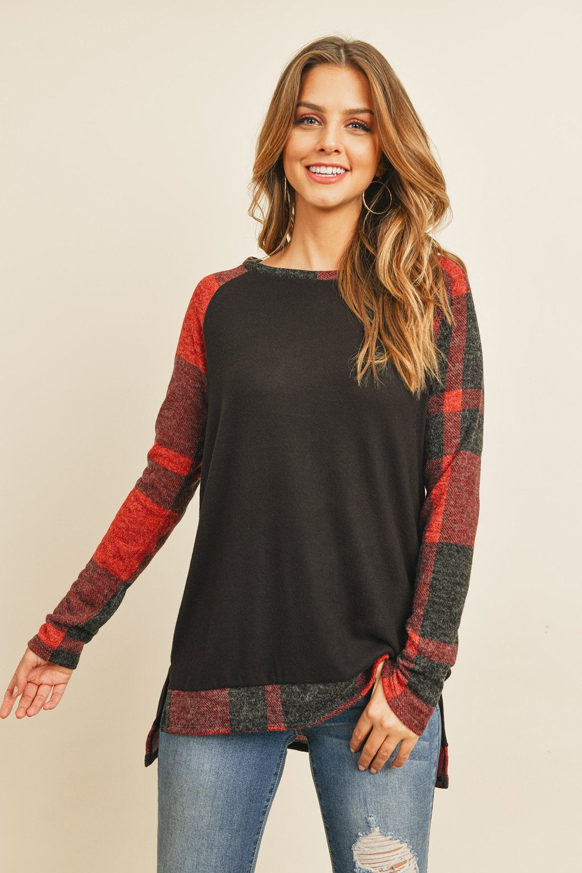 A woman in a Riah Fashion Brush Hacci Plaid Contrast Long Back Hem Top with red and beige accents, paired with blue ripped jeans, stands against a plain background.