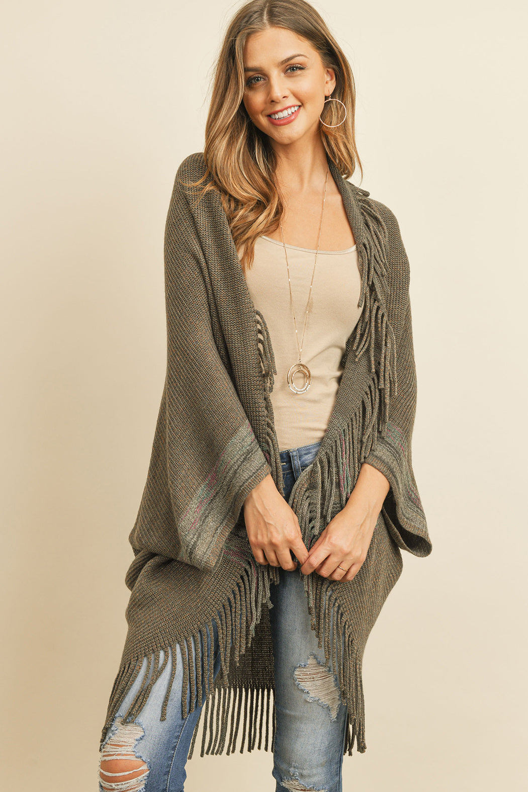 Someone is wearing a Fringe Stripe Open Front Kimono by Riah Fashion over a beige top and ripped jeans, standing against a plain background.