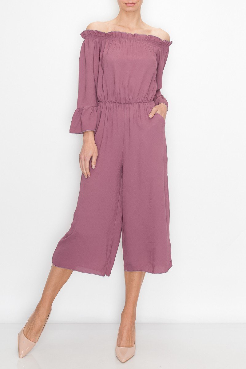 A person in a Stylespect Off Shoulder Jumpsuit - Mauve with bell sleeves and neutral heels poses against a plain white background.
