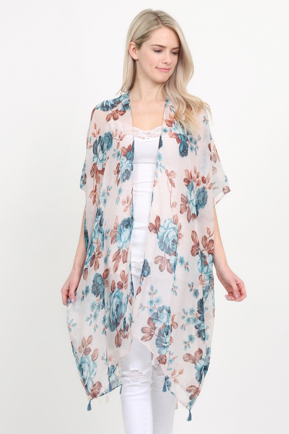 A woman stands against a plain background, wearing a Riah Fashion beige blue open front knee-length floral cardigan over a white outfit.