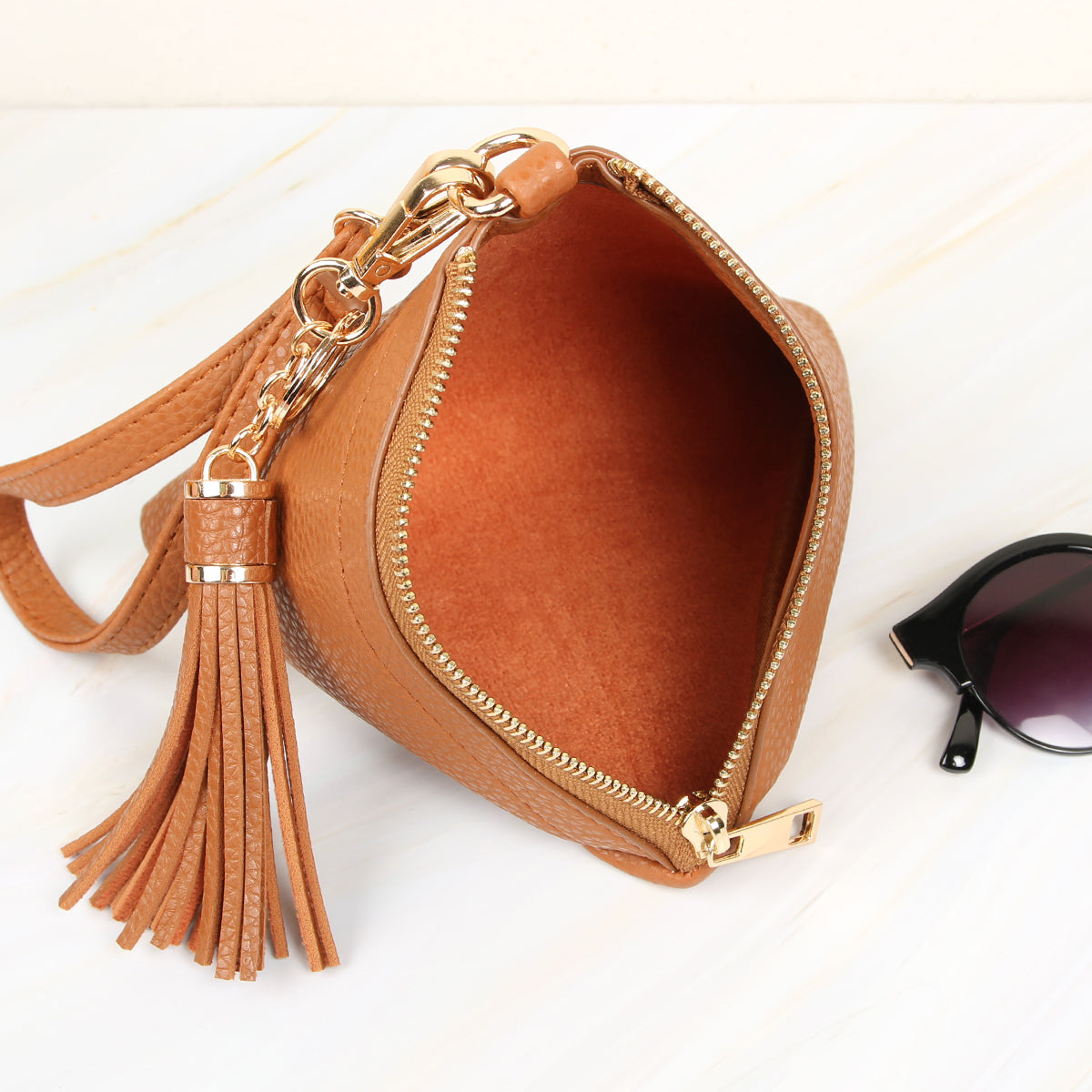 A person in a white shirt and jeans is holding the Riah Fashion Pyramid Shape Tassel Wristlet Leather Bag in orange.