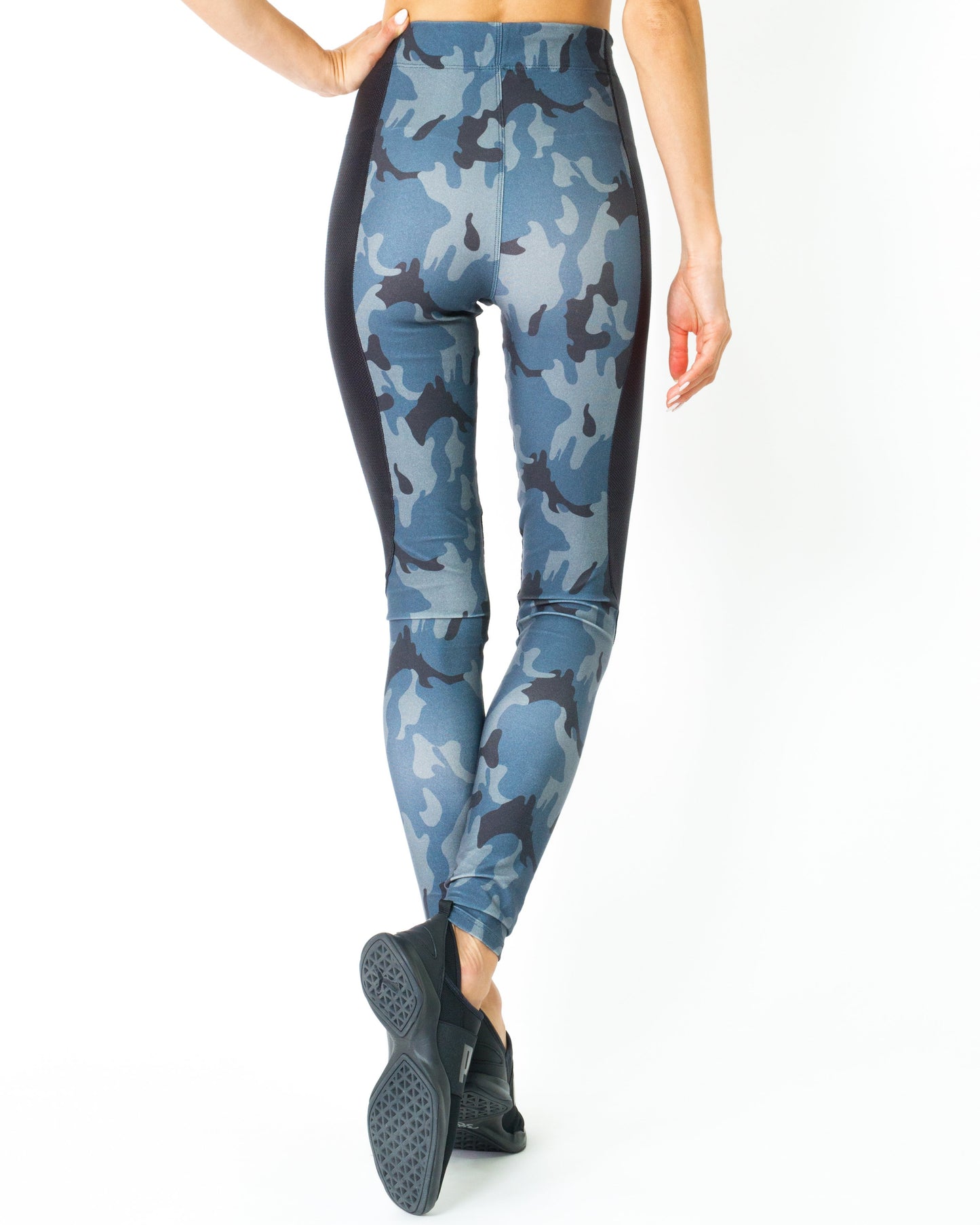 Wearing the Veloso Supplex Moisture-Resistant Fashion Leggings & Sports Bra Set by Savoy Active, a person in camo-patterned workout attire poses indoors with one hand on a swinging chair.