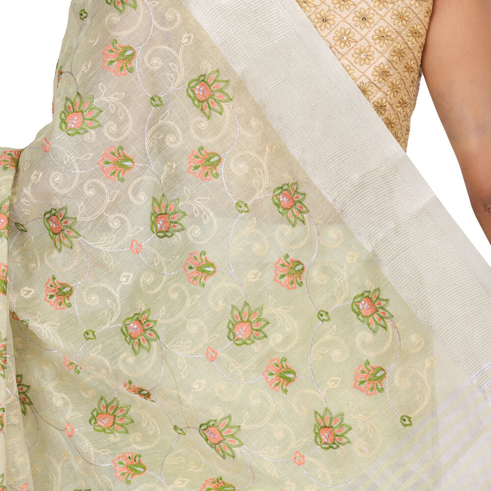 A woman in Chiros Tissue Banarasi Saree With Embroidery - Sea Green stands indoors on a wooden floor, against a decorative wall.