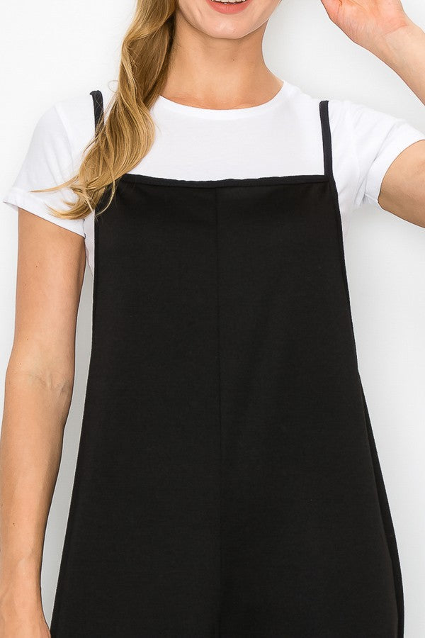 A person models the Stylespect Cropped Bottom Wide Leg Oversized Jumpsuit in black, paired with a white t-shirt and white sneakers, set against a plain white backdrop.