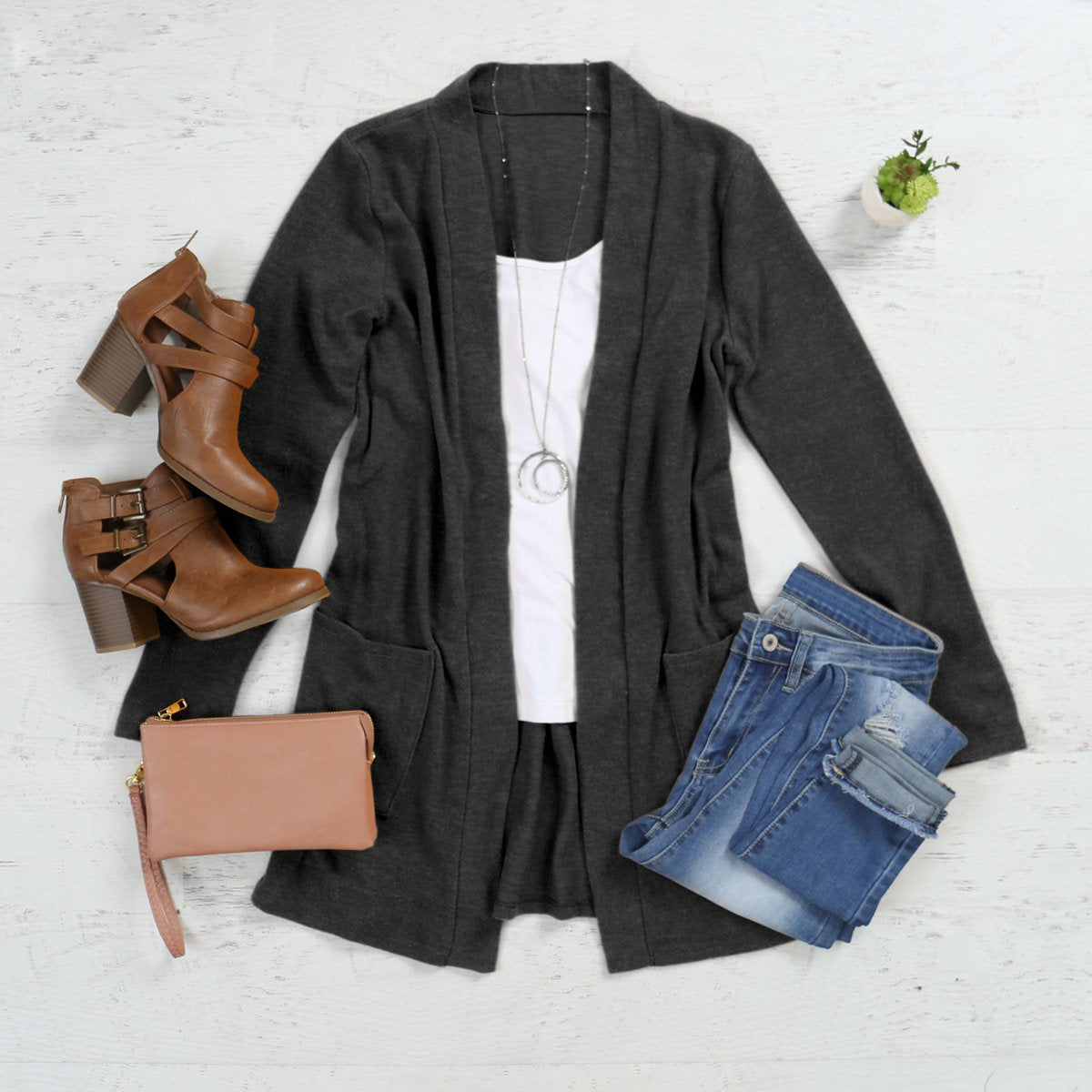 A woman in a Brushed Melange Open Front Cardigan by Riah Fashion and ripped jeans stands against a pink background, hands in her pockets.