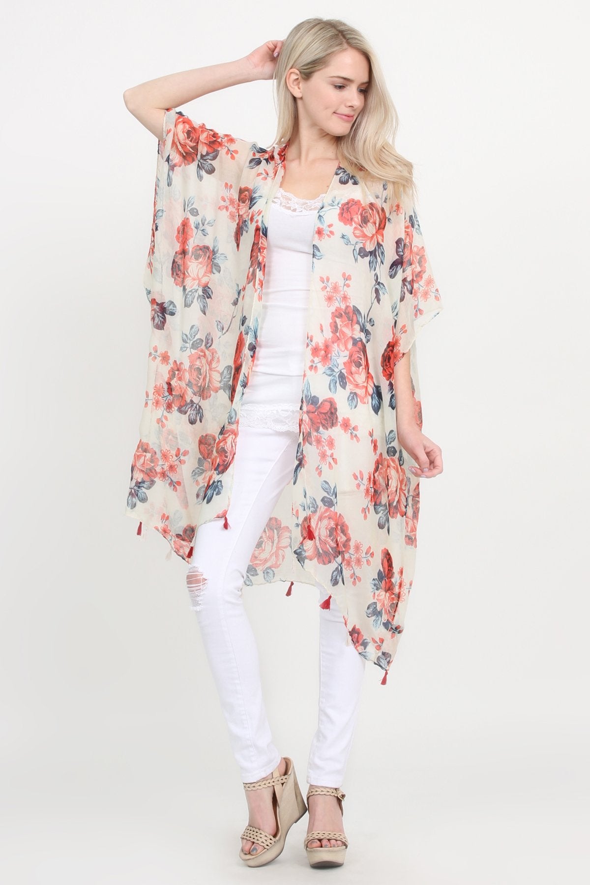 A woman stands against a plain background, wearing a Riah Fashion beige blue open front knee-length floral cardigan over a white outfit.