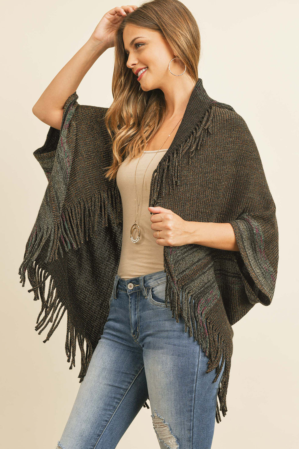 Someone is wearing a Fringe Stripe Open Front Kimono by Riah Fashion over a beige top and ripped jeans, standing against a plain background.