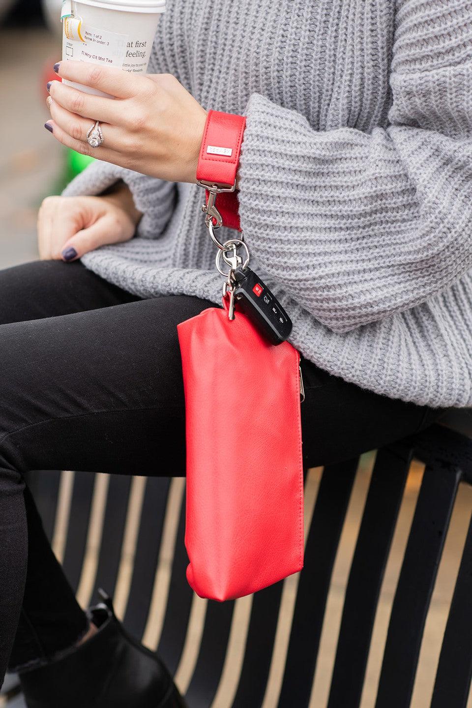 A red vegan leather wristlet set from KEYPER, featuring a gold zipper and detachable strap with gold hardware.