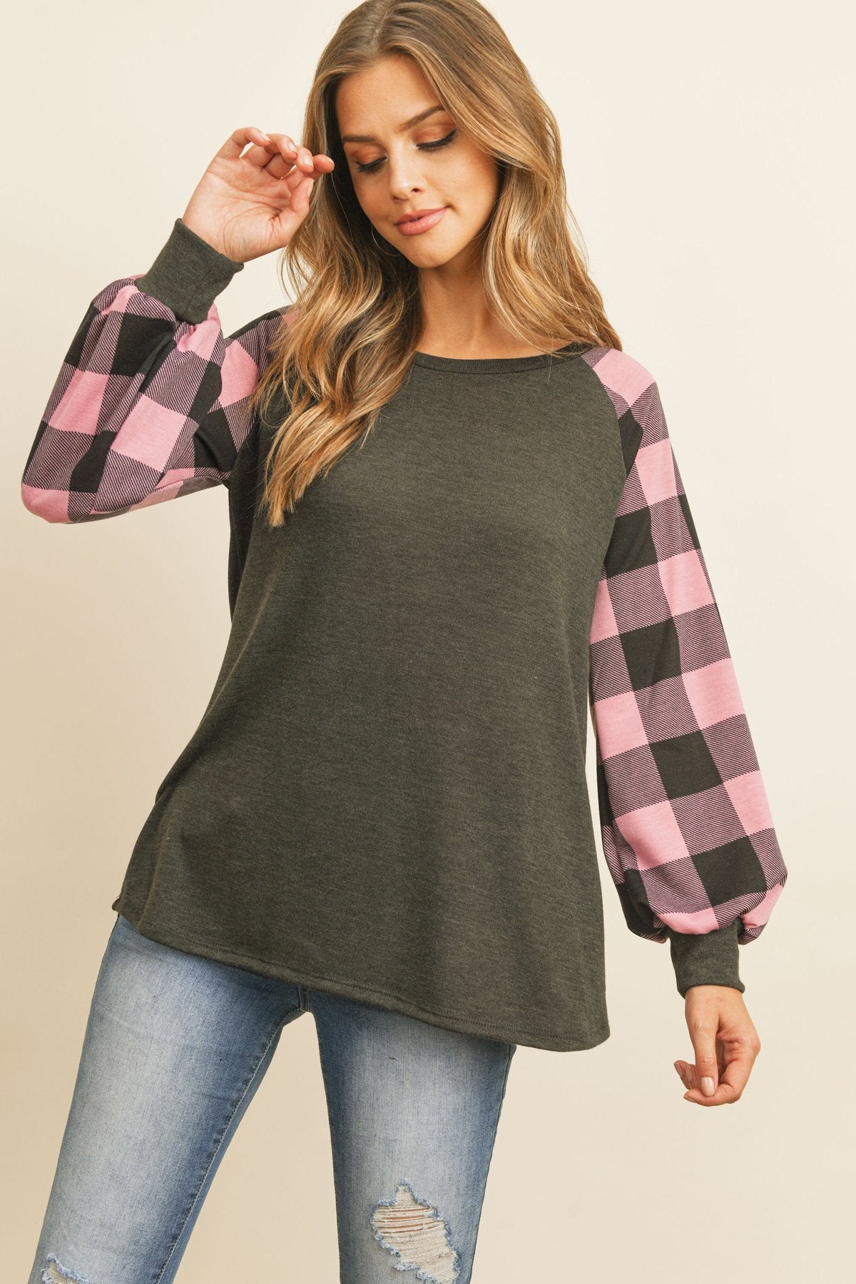 A woman wearing a faded denim plaid puff sleeved round neck top by Riah Fashion and ripped jeans stands against a plain background.