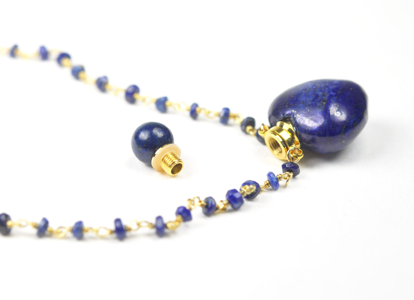 The Gena Myint Lapis Lazuli Heart Necklace features a blue beaded design with a heart-shaped pendant and gold chain clasp.