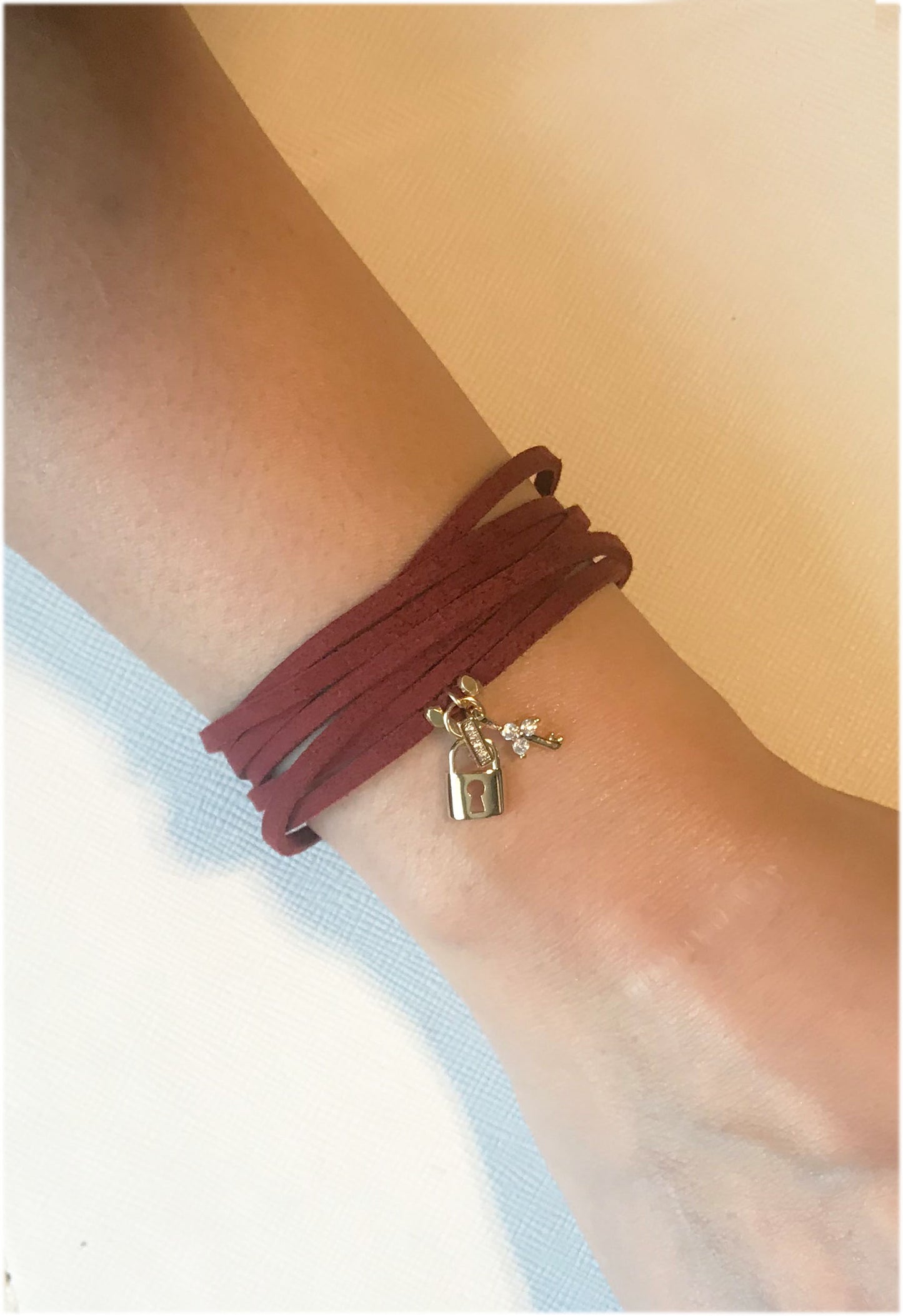 A burgundy suede wrap bracelet by Gena Myint, featuring a gold robot and silver key charm.