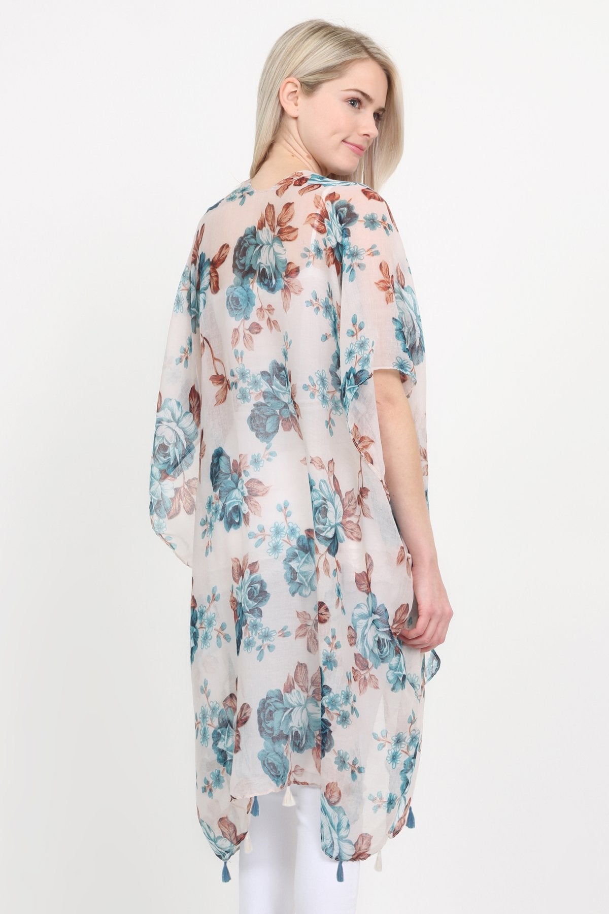 A woman stands against a plain background, wearing a Riah Fashion beige blue open front knee-length floral cardigan over a white outfit.