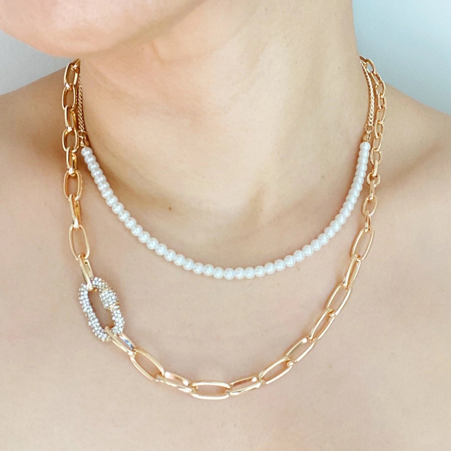 A person wearing the Ellison + Young Classic Duo Layered Pearl Necklace Set with gold links and pearl accents, plus a simple strand of pearls.