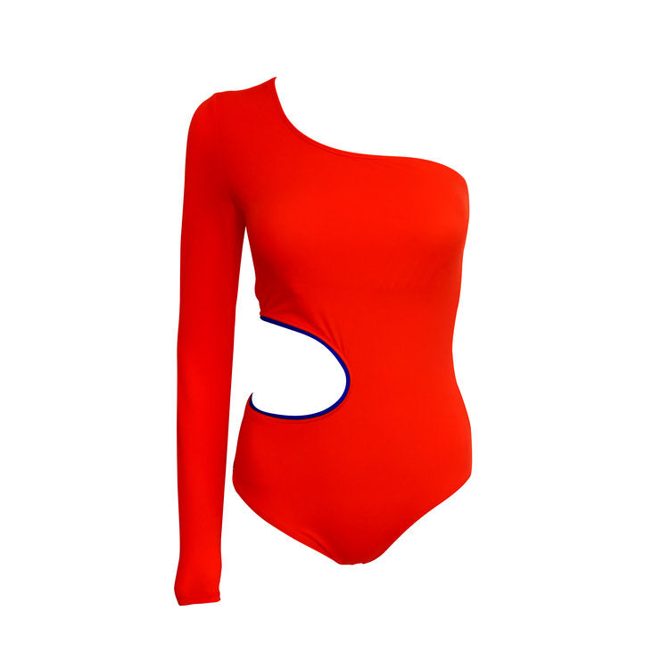 Someone wearing the Waves asymmetrical swimsuit by Mirame poses on a bed in front of a window.