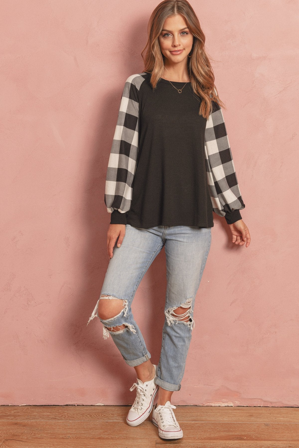 A woman wearing a faded denim plaid puff sleeved round neck top by Riah Fashion and ripped jeans stands against a plain background.