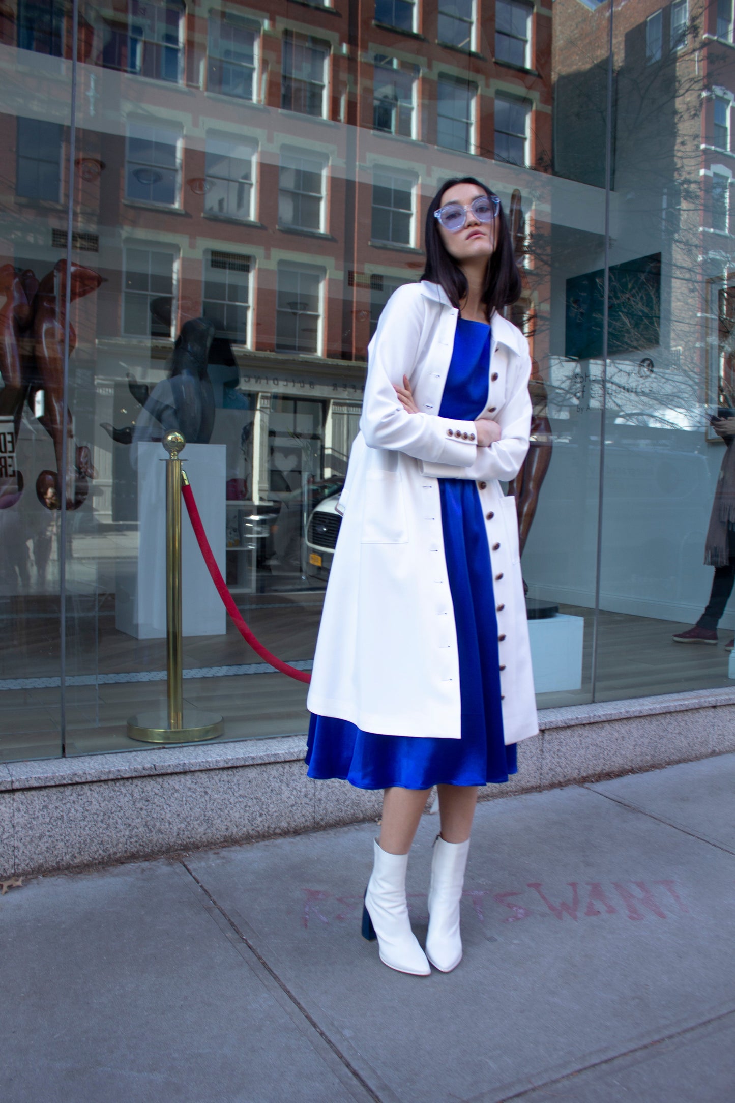 The Monique White Coat by Le Réussi® is a long-sleeve trench coat featuring a collar, button closure, matching belt, and cuff buttons.