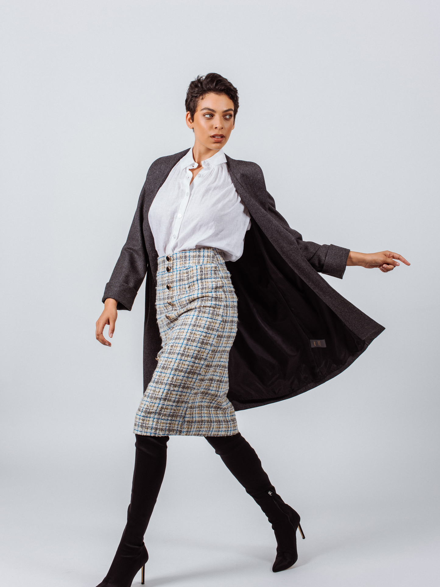 A person poses in a dark dress and the Power Woman Worsted Flannel Long Jacket in Dark Grey by Le Réussi®, against a white background, wearing black high heels.