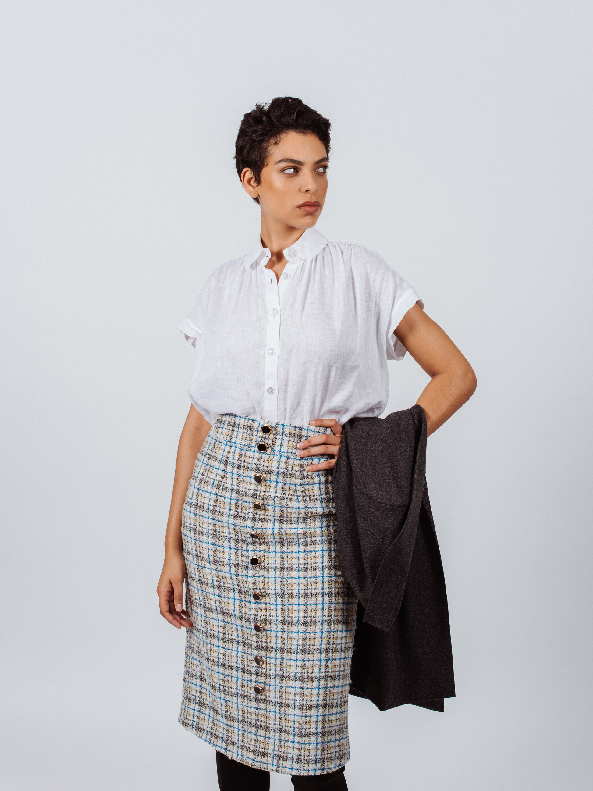 A person is wearing the Power Woman- Eye Catching Tweed Skirt by Le Réussi®, a high-waisted, button-down plaid skirt in blue, beige, and white, paired with a white blouse.