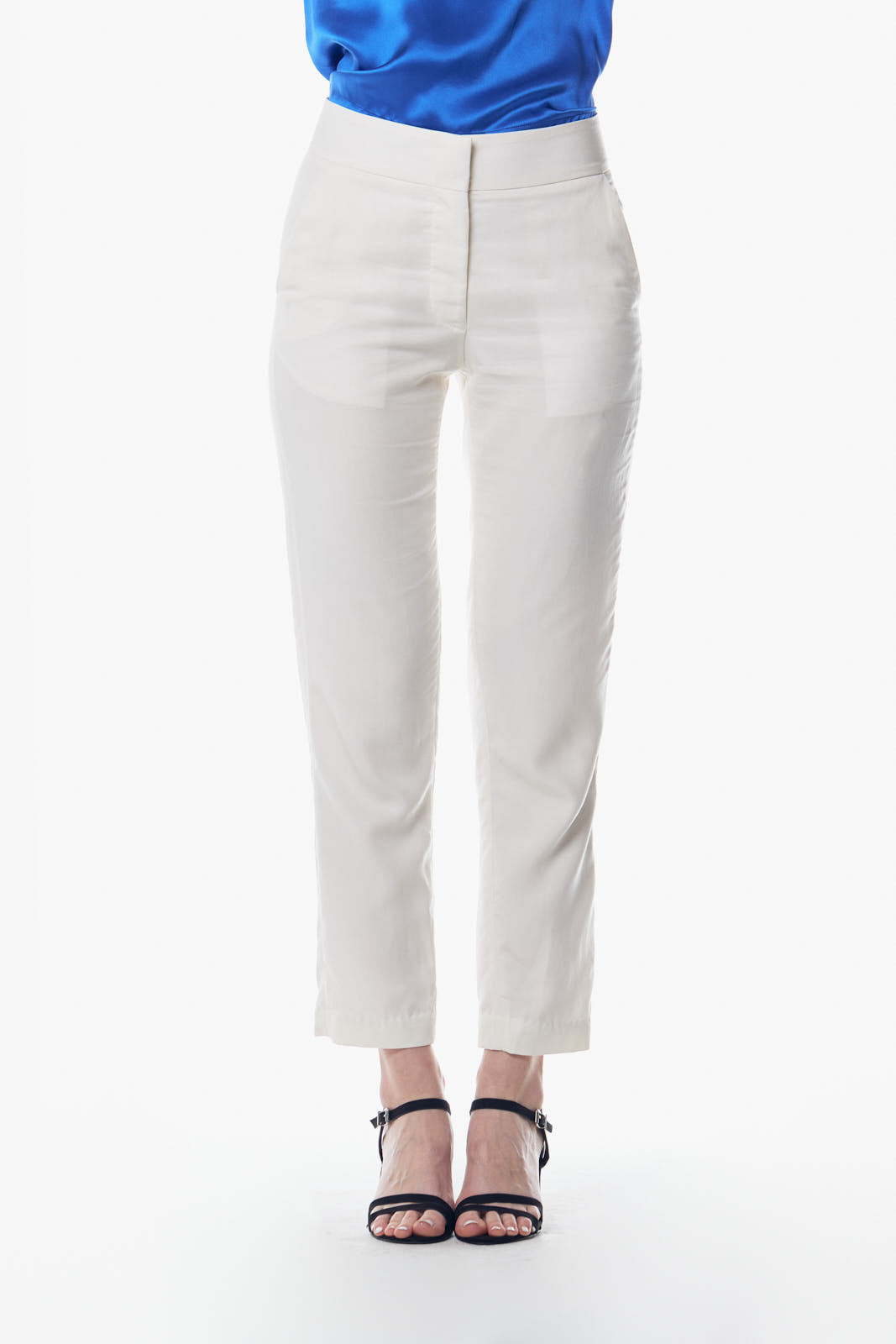 A person is wearing Le Réussi® White Skinny Pants and black strappy sandals, standing against a white background. Their blue top is partially visible.