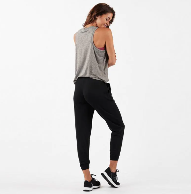 A woman models indoors in Savoy Actives Finnley Jogger Pant with a drawstring waist in black, pairing it with a crop top, her hands resting in the pockets.