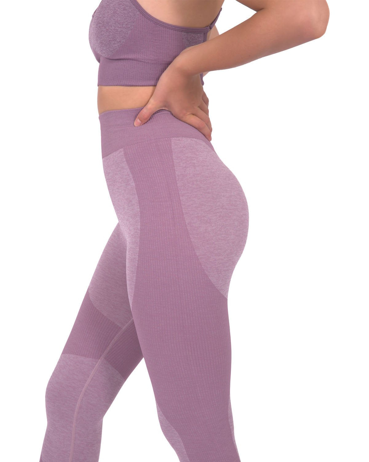A person in Savoy Actives Megara Seamless Legging With Striped Panels - Purple and black sneakers stands outside a building featuring large glass doors and tropical plants.