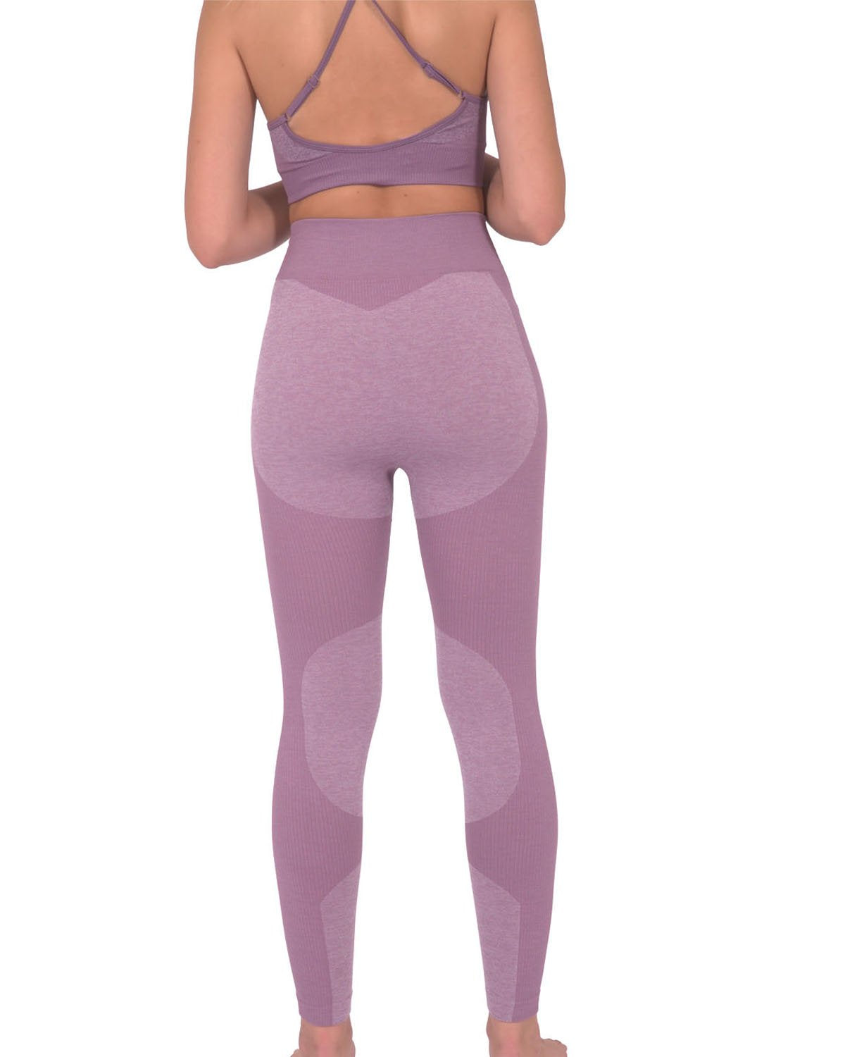 A person in Savoy Actives Megara Seamless Legging With Striped Panels - Purple and black sneakers stands outside a building featuring large glass doors and tropical plants.