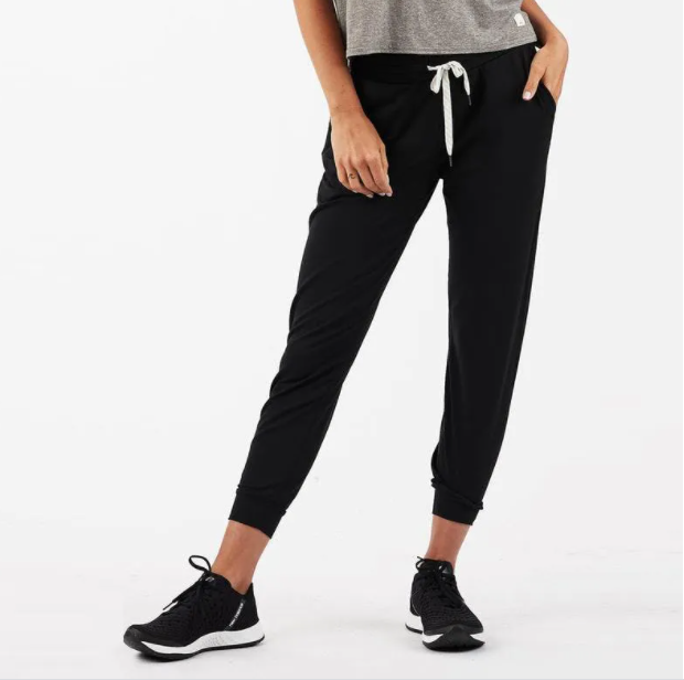 A woman models indoors in Savoy Actives Finnley Jogger Pant with a drawstring waist in black, pairing it with a crop top, her hands resting in the pockets.