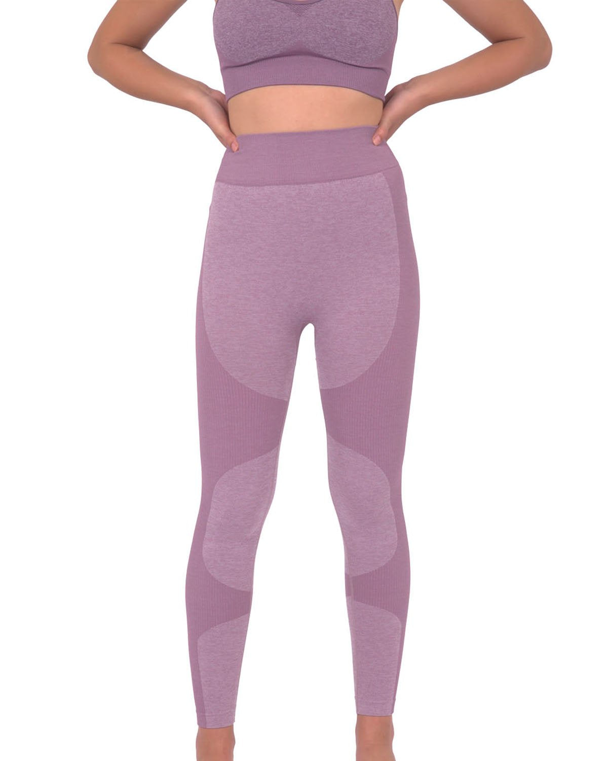 A person in Savoy Actives Megara Seamless Legging With Striped Panels - Purple and black sneakers stands outside a building featuring large glass doors and tropical plants.