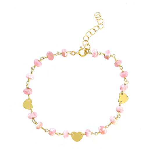 The Pink Rhodocrosite and Heart Charm Bracelet by Gena Myint is a gold chain bracelet with pink stones, three heart-shaped charms, and an adjustable clasp.