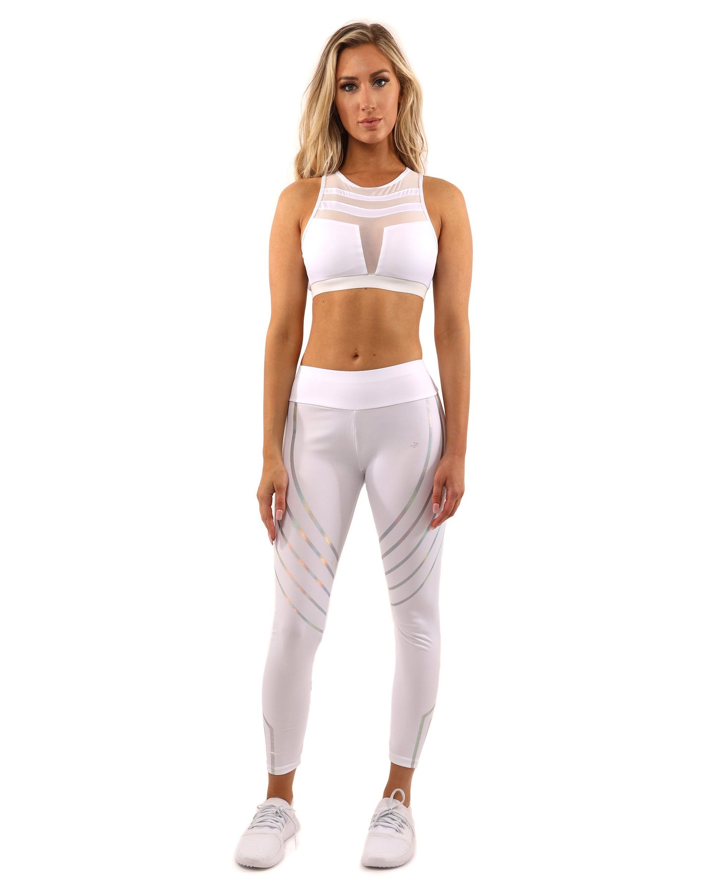 A person is standing with one hand on their hip, wearing a white sports bra, Laguna Leggings - White by Savoy Active, and white sneakers.