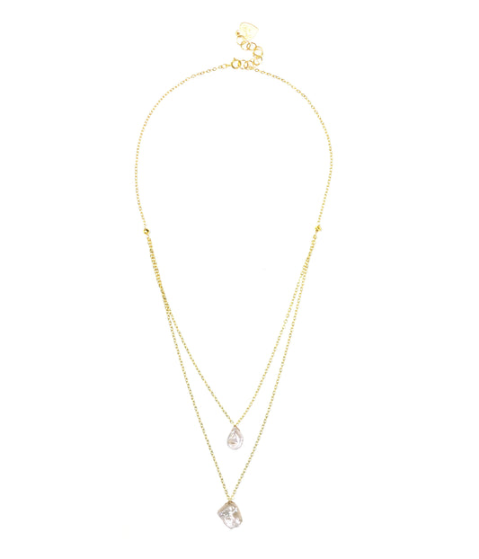 The Keshi Pearl Layered Necklace by Gena Myint is a gold double-layer necklace featuring two clear gemstone pendants: one pear-shaped and the other rectangular.