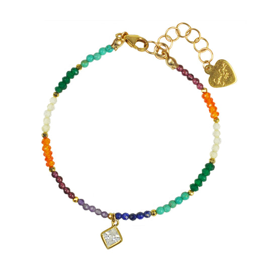 The Chakra With Clear Quartz Drop Bracelet by Gena Myint features colorful beads in green, orange, white, purple, and dark red. It includes a gold clasp, heart charm, and square pendant.