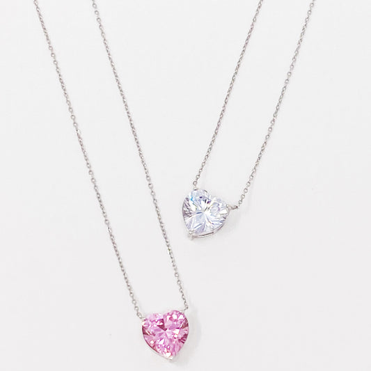 Two Absolute Beauty sterling silver heart necklaces by Ellison + Young; one with a pink gem, the other with a clear gem, against a white background.