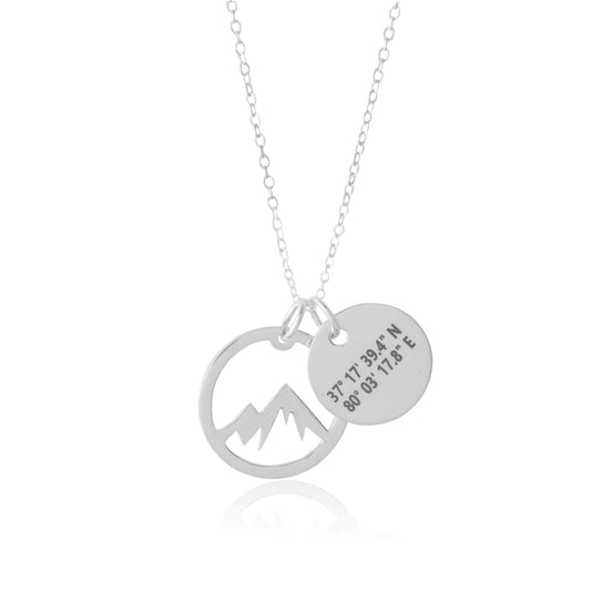 The Coordinate Mountain Necklace by Sincerely Silver is a silver piece featuring a mountain design pendant and a round one engraved with coordinates.