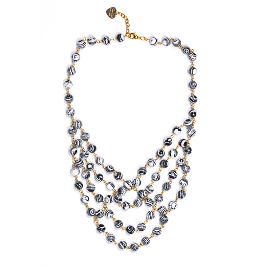 The Gena Myint Zebra Stripe Turquoise Statement Necklace features multi-strand black and white swirled beads with gold links, displayed on a white background.