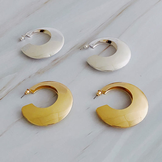 On a marble surface, four round Light and Modern Hoop Earrings from Ellison + Young are displayed, with two in silver and two in gold.