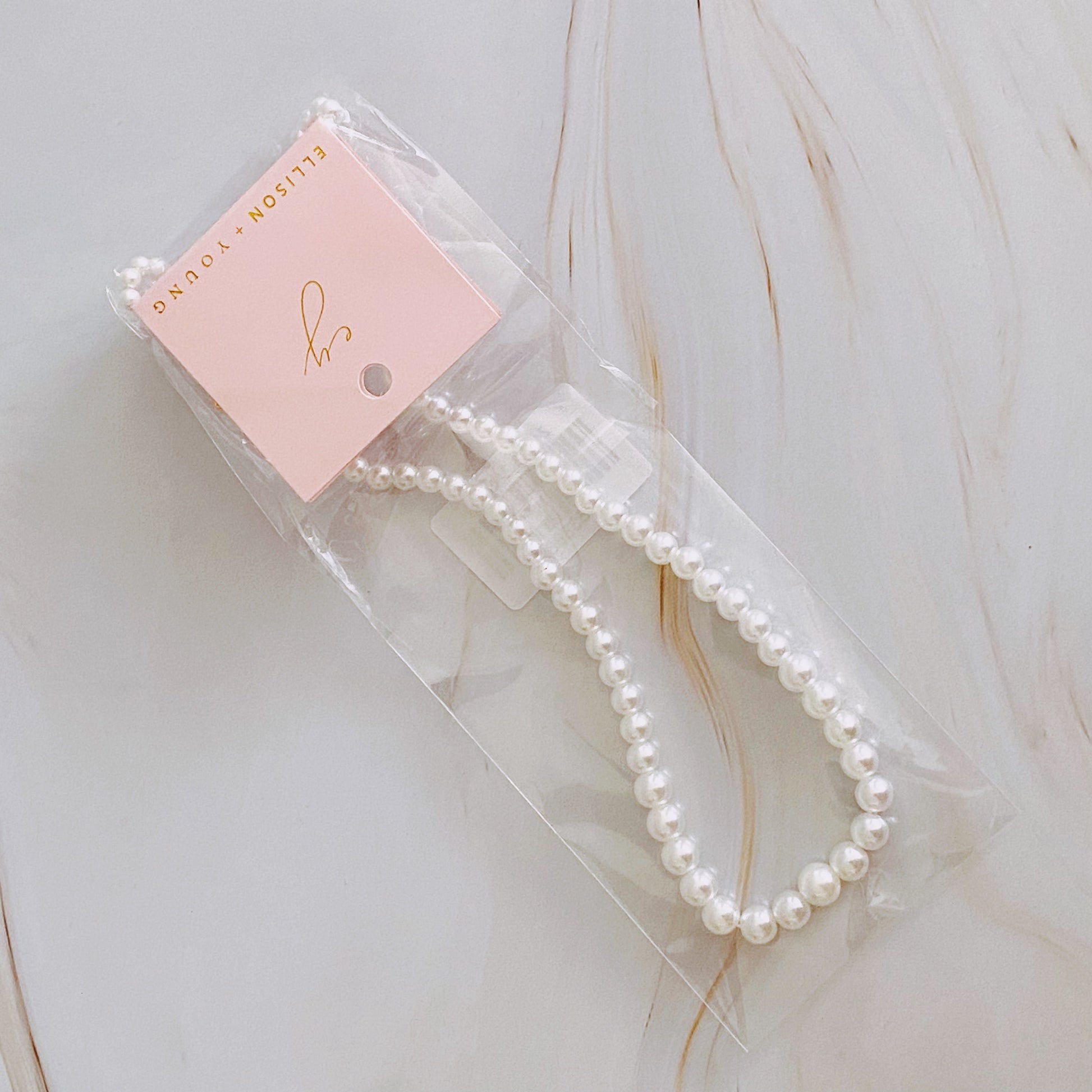 The Queen Liz Graduated Pearl Necklace by Ellison + Young features white pearls with a gold clasp, displayed on a light marble surface.