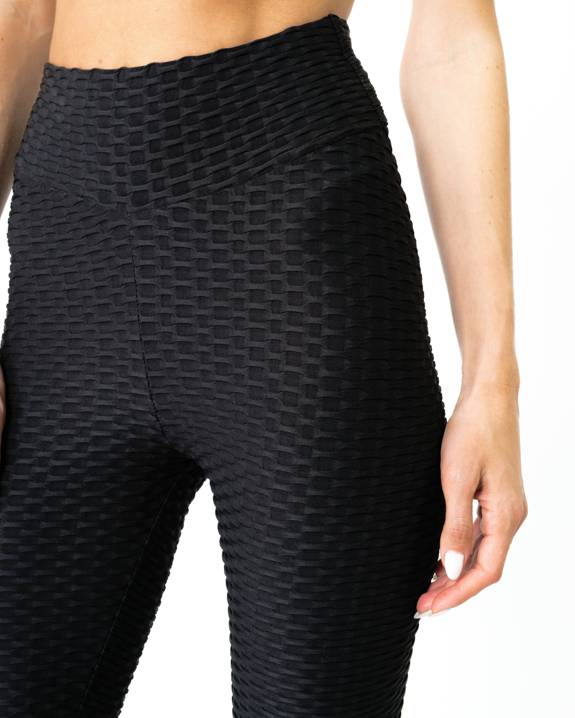 A person in Savoy Actives Bentley Leggings - Black stretches outdoors on a tree-lined paved path with benches.