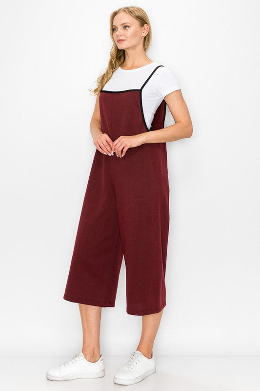 A person is wearing a white T-shirt and the Cropped Bottom Wide Leg Oversized Jumpsuit in Burgundy from Stylespect, standing against a plain white background.