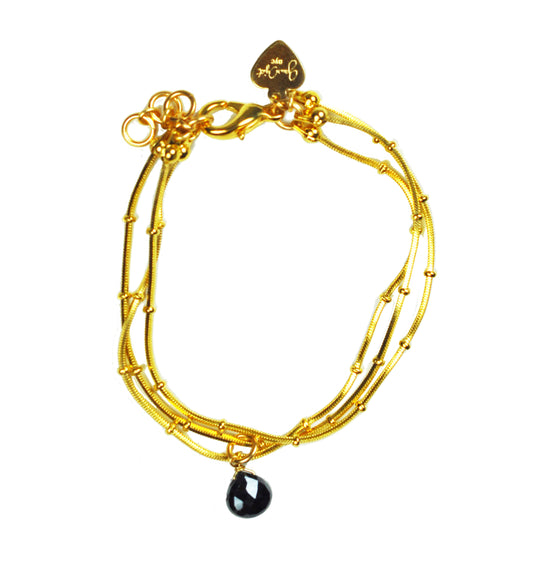 Gena Myints Black Spinel Drop Ball Chain Bracelet features an adjustable gold chain, a small black spinel pendant, and a branded charm.