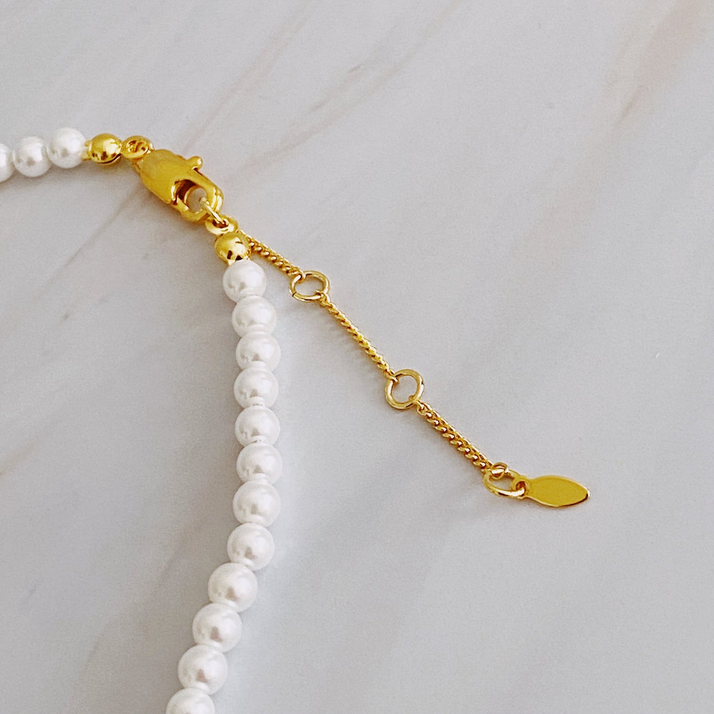 The Queen Liz Graduated Pearl Necklace by Ellison + Young features white pearls with a gold clasp, displayed on a light marble surface.