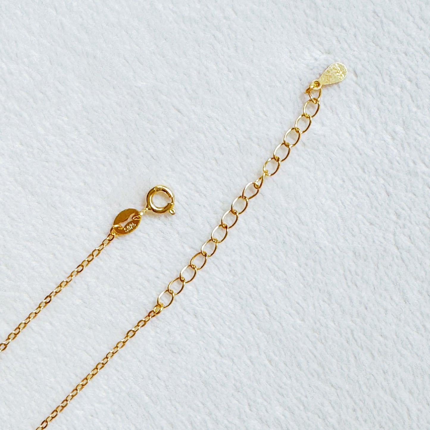 The Shine Classy Bow Sterling Silver Necklace by Ellison + Young, dipped in gold, is showcased on a card reading Fine Jewelry Collection and placed on white pebbles.